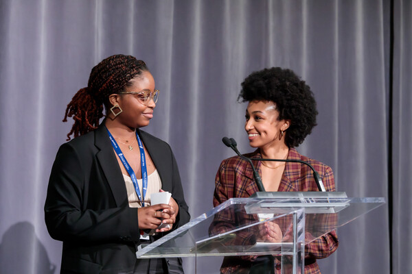 Two women at a podium looking at each other and smiling