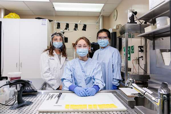 A group of three women standing in a pathology lab