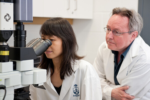 a man watching while a woman looks into a microscope