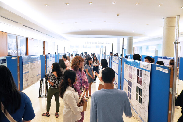 Students and faculty gather in a large room to look at research posters