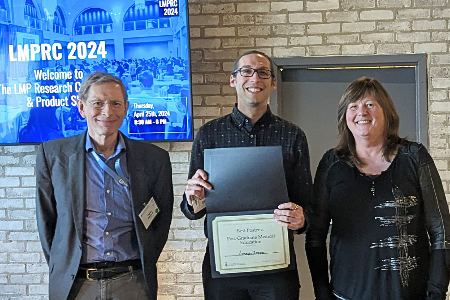 Three people are standing indoors. The person in the middle, Joseph Zeppa holding a certificate, is flanked by two others, Myron Cybulsky and Janice Robertson. Behind them is a digital screen displaying "LMPRC 2024," event details, and an image of a crowded meeting room. They are at the awards ceremony of the LMPRC. 
